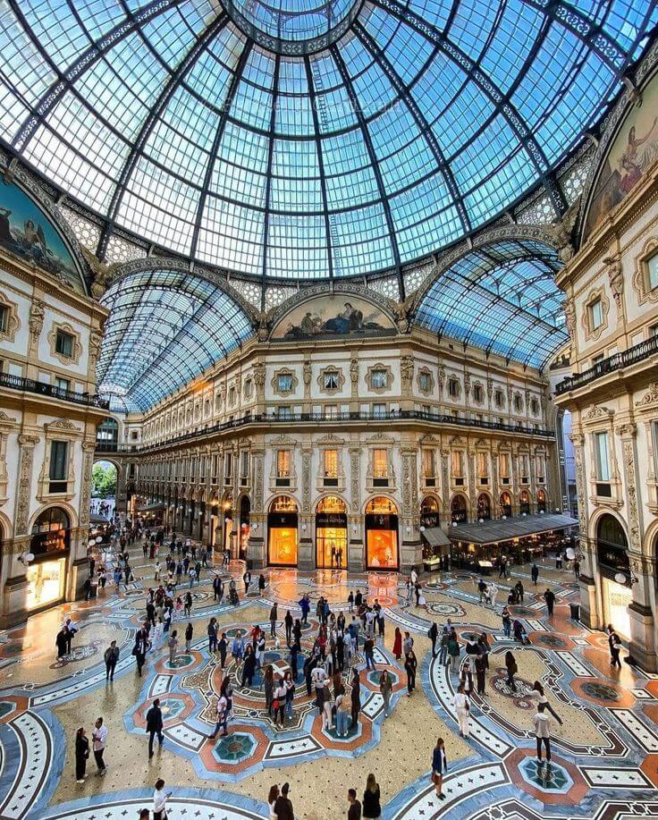 Interior Galleria Vittorio Emanuele II di Milan, Italia, dengan langit-langit kaca yang megah, lantai marmer yang indah, dan deretan butik mewah di kedua sisinya, menciptakan suasana elegan dan bersejarah di pusat kota Milan.